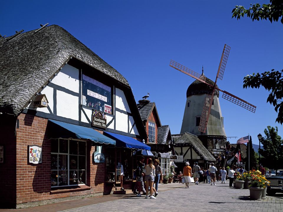 A thatched, half-timbered shop on a Solvang street with a Danish windmill behind it and visitors walking past